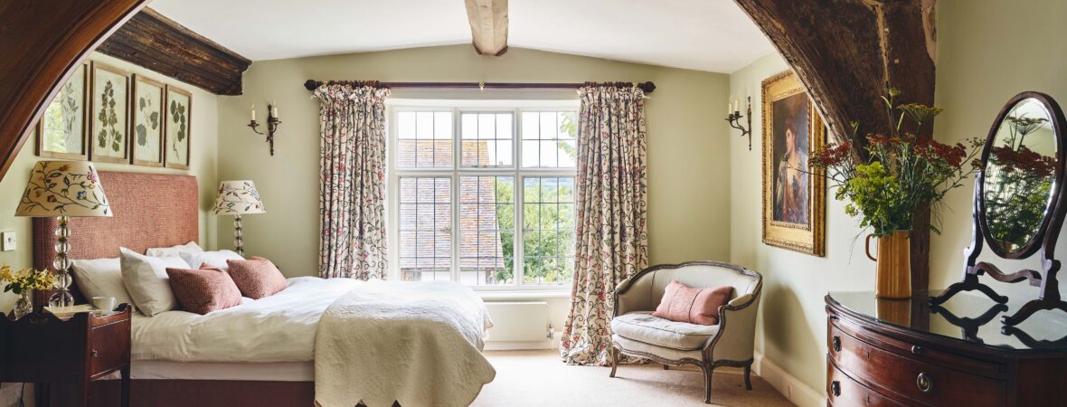 Spacious bedroom in a large holiday house, featuring rustic beams, a cosy bed, and a bright window, perfect for family stays and welcoming pets for a relaxing getaway