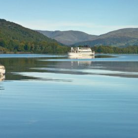 Derwentwater Lake in winter, featuring snow-dusted hills and a calm, icy lake reflecting the clear blue sky