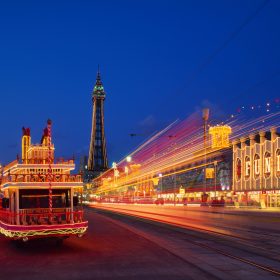 A vintage trolley car with illuminated front lights, creating a charming scene in the evening ambiance with Blackpool Tower in the background