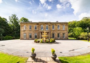 The impressive front view of a large mansion, showcasing a central fountain and beautifully landscaped grounds