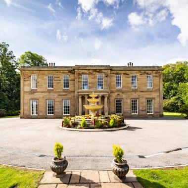 The impressive front view of a large mansion, showcasing a central fountain and beautifully landscaped grounds