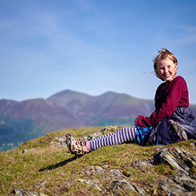 Woman sat on a hill with Cumbrian landscape behind her.