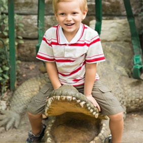 Small boy sitting on the crocodile monument in the zoo.