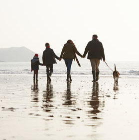 Family walking along a beach with a dog.