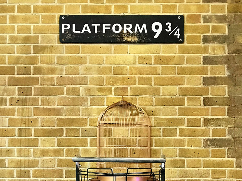 Sign with Platform 9 3/4 on it, above a trolley with suitcases.