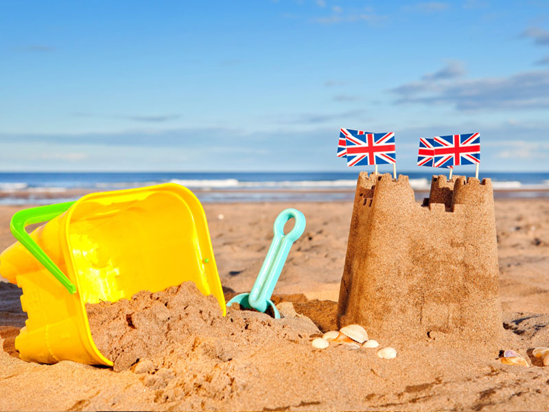 British Seaside traditional sand castle on the beach with bucket and spade shells and Union Jack Flags.