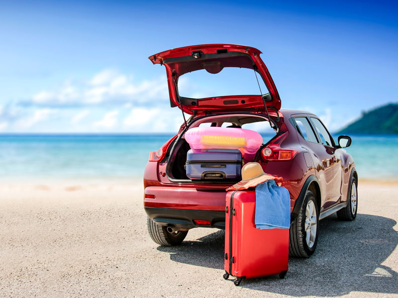 Summer time and red car on beach with few suitcase.