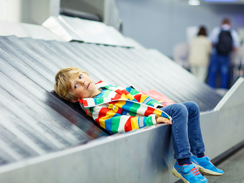 Child waiting with kids suitcase on baggage carousel. 