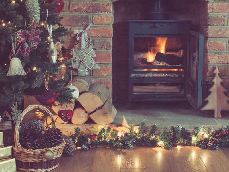 Decorated fireplace with woodburner, lit up Christmas tree.