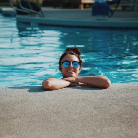 Four individuals relax together in a swimming pool, enjoying the sun and water in a serene setting