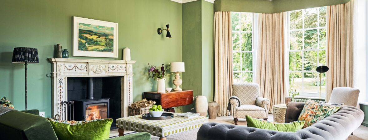 A stylish living room in a large holiday cottage adorned with green walls and a charming open fire, perfect for relaxation and taking time away from everyday life