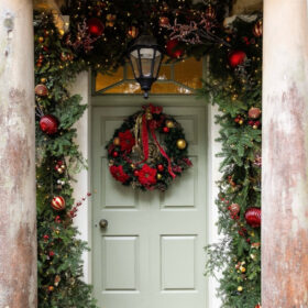 A green door adorned with a festive wreath featuring red and gold decorations, creating a welcoming holiday atmosphere